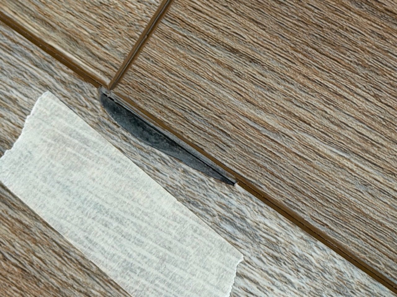 Edge chipping at an LVP plank joint next to a torn paper label