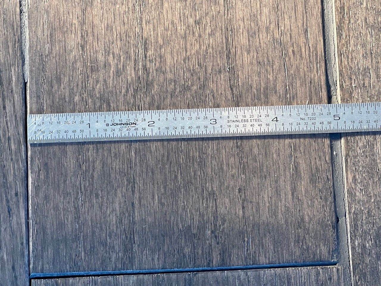 Steel ruler measuring a board gap during a hardwood flooring inspection